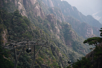 Naklejka premium Cable car through the mountains to arrive at the Yellow Mountain in Huangshan, China, with view of the city in the background on a foggy day of autumn