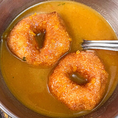 Close up of South Indian Breakfast Food Medu Vada placed on bowl of Sambar