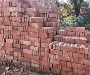 Tall stacks of red and brown clay bricks neatly arranged at a construction site, showcasing the raw materials ready for building projects and construction work.