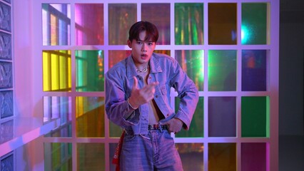Close up of asian performer with sun glasses moving freestyle dance while looking at camera at nightclub. Happy street dancer dancing and show footstep with colorful bright neon light. Regalement.