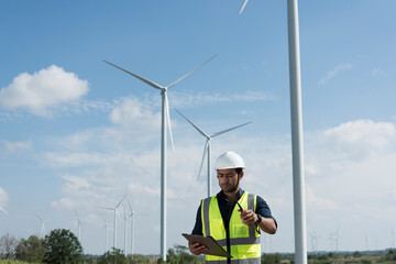 Male engineers with drawing against turbines on wind turbine farm.
