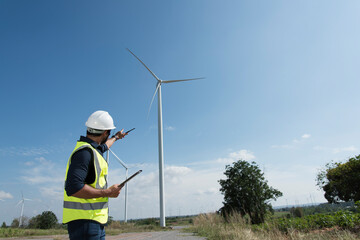 Male engineers with drawing against turbines on wind turbine farm.