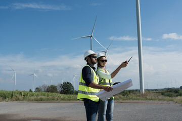 Couple engineers with drawing against turbines on wind turbine farm.
