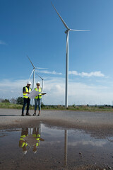 Couple engineers with drawing against turbines on wind turbine farm.
