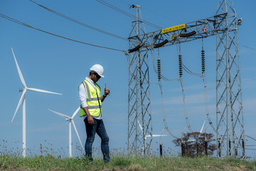Male engineers with drawing against turbines on wind turbine farm.