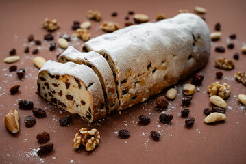 Sliced Stollen. Traditional cake Stollen dusted with powdered sugar with dried fruits and nuts on a brown background.