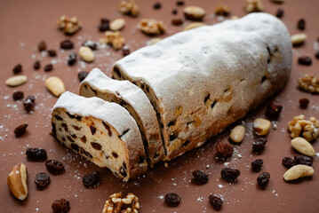 Sliced Stollen. Traditional cake Stollen dusted with powdered sugar with dried fruits and nuts on a brown background.