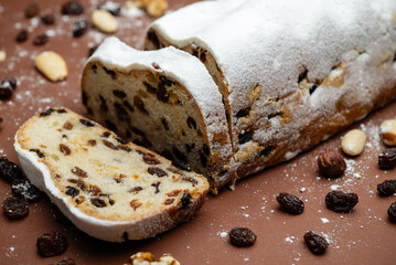 Sliced Stollen. Traditional cake Stollen dusted with powdered sugar with dried fruits and nuts on a brown background.