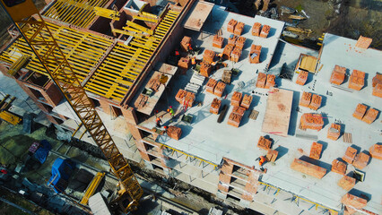 Obraz premium Construction site with crane and workers laying bricks. A high-angle view of a construction site with workers actively laying bricks.