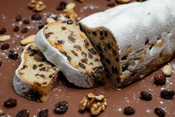 Sliced Stollen. Traditional cake Stollen dusted with powdered sugar with dried fruits and nuts on a brown background.