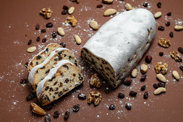Sliced Stollen. Traditional cake Stollen dusted with powdered sugar with dried fruits and nuts on a brown background.