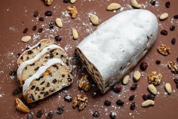 Sliced Stollen. Traditional cake Stollen dusted with powdered sugar with dried fruits and nuts on a brown background.
