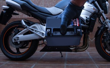 A hand with black latex gloves holds a motorcycle battery. A motorcycle in the background. Maintenance and spare parts concept.