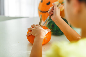 Boy making jack o lantern at home white kitchen, cutting real pumpkins and playing with paper black...