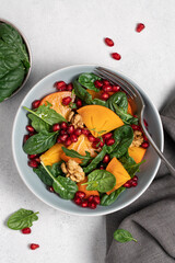 Persimmon salad with pomegranate seeds, spinach and walnuts in bowl on white background with copy space. New Year and Christmas menu