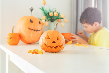 Boy making jack o lantern at home white kitchen, cutting real pumpkins and playing with paper black...