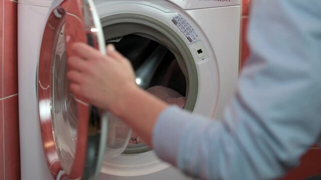 Close-up of person opening door of washing machine, preparing to remove clean laundry. for household chores, laundry, and home appliance themes. opening door of washing machine remove clean laundry