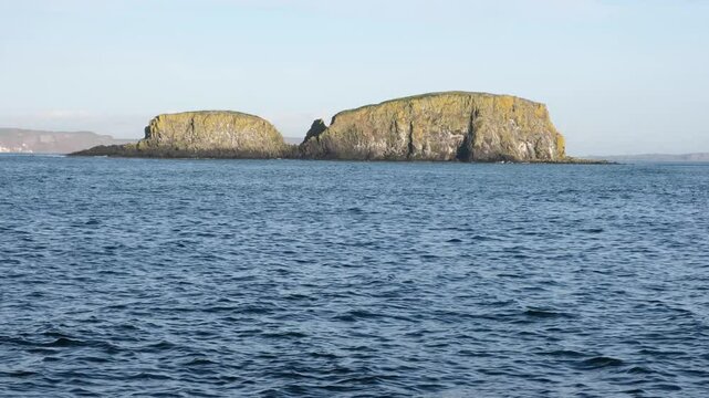 Rugged landscape of Sheep Island on the Causeway Coast of Northern Ireland surrounded by clear blue ocean and bright sky on fresh winter day, no people.