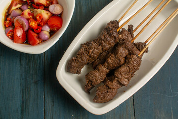 Maranggi satay on white plate over dark background with Indonesia sweet soy dipping sauce (sambal kecap)