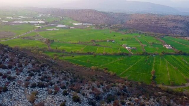 A sweeping aerial drone view over a lush patchwork agricultural valley bordered by dramatic, rugged rocky cliffs.