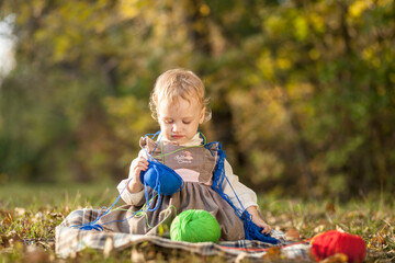 Little girl playing with woolen balls of threads of different colors in autumn park