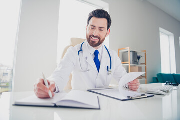 Photo of experienced doctor guy sit table hold paper check list write copybook in hospital room