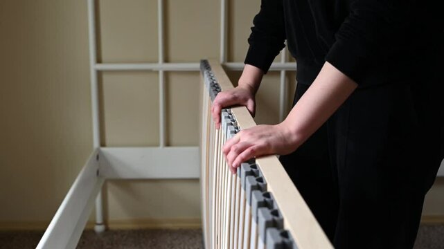 The girl takes a wooden bed frame in her hands and tries to put it in the right place.
