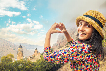 Happy young tourist look at camera and pose hands form heart against panorama view of Noravank...
