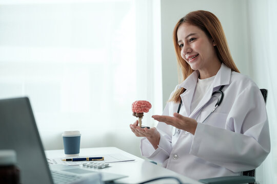 A woman in a white lab coat is holding a brain model