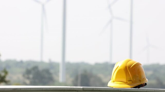 Wind Turbine Construction Site: A yellow hardhat rests atop a metal beam in front of a row of wind turbines, symbolizing progress, sustainability, and the future of energy. 