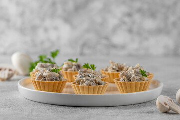 Mini tartlets with mushrooms in a cream sauce, with cheese, garlic and herbs on a white plate on a gray concrete background.
