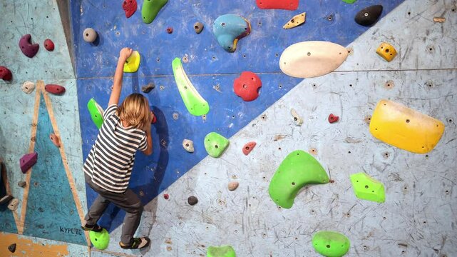6-year-old boy practicing bouldering on a colorful indoor climbing wall. Focused and determined, he navigates different holds, showcasing strength and balance.