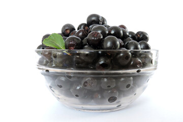 Fresh aronia berries decorated with a green leaf in a glass bowl, white background, side view