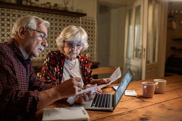 Elderly couple managing finances online with laptop and receipts
