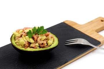Ripe avocado with shrimps. Tasty and festive appetizer on black slate isolated on white background.