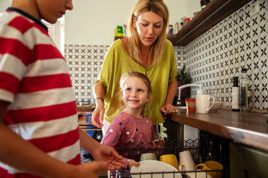 Mother teaching kids to load the dishwasher as part of family chores