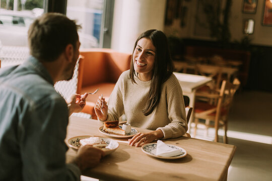 A joyful couple enjoys coffee and pastries in a cozy cafe during a sunny afternoon
