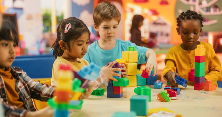 Group of Adorable Creative Kids Using Colorful Building Blocks to Play Together. Cheerful Female Teacher Spending Productive Time in Daycare, Teaching Multiethnic Kids in Preschool