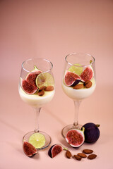 delicate dessert with figs and almonds in a glass on a high stem. Pink background.