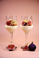 delicate dessert with figs and almonds in a glass on a high stem. Pink background.