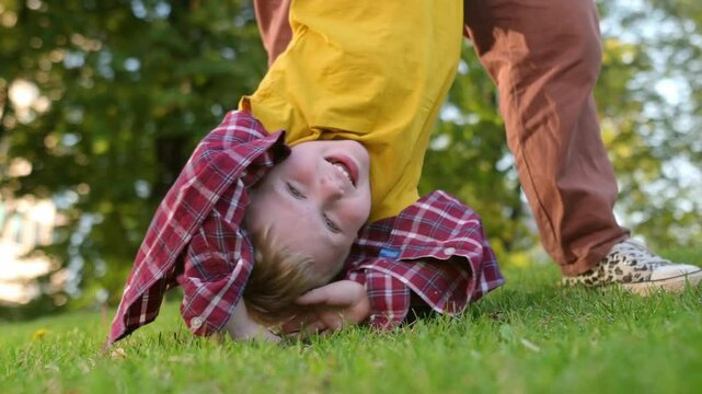 Mom and her little son are having fun together in a city park on a warm summer evening. Active family. Mom swings happy laughing boy upside down. Quality time and activity for mom and her child