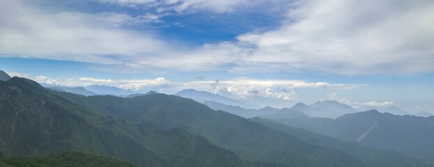 Panoramic view of lush green mountains under a vibrant blue sky with scattered clouds