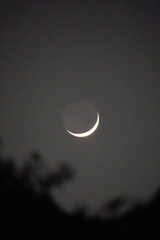 Small white part of growing moon and lightly visible full moon, moon watching, vertical © Anna
