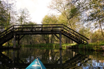 Fototapeta premium Kanutour auf den Fließen im Spreewald mit Blick auf eine Holzbrücke und wunderschöner Spiegelung im Wasser