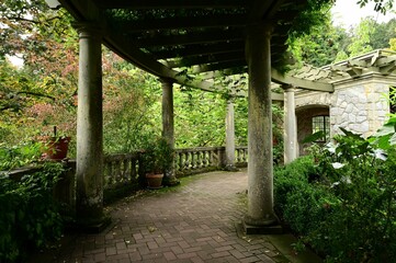 Naklejka premium Serene stone walkway with columns surrounded by lush greenery in a garden
