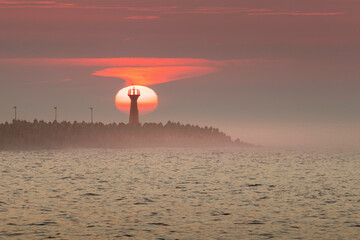 Tranquil Ocean Sunset With Vibrant Shades of Orange and Misty Horizon and coastline with lamp