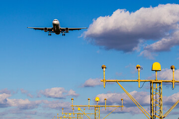 Airplane Approaching Runway Under Vibrant Blue Sky with Clouds and Airport Lighting Structures