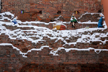 Red brick wall is lightly covered with snow. Puppets. Toruń, Poland.