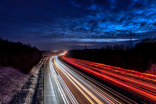 Lichtspuren der Fahrzeuge auf einer Autobahn - der A81 - welche bis tief in den Horizont reichen und dort den Himmel erhellen. Winterliche Stimmung. Schnee.
