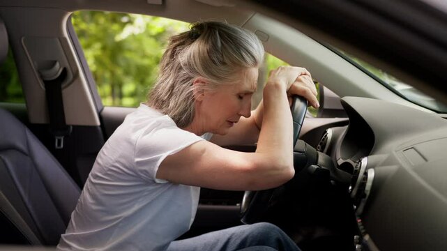 Despair stressed crying unhealthy Caucasian elderly aged senior woman female mature car driver auto owner grandmother lean on steering wheel pain traffic accident problem trouble in automobile at city